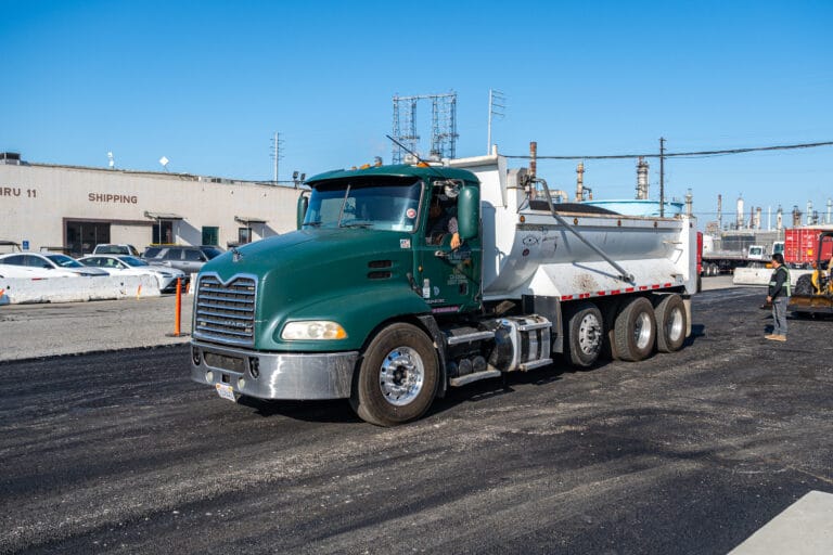 Green dump truck on asphalt surface, transporting materials for driveway paving in Anaheim, California.